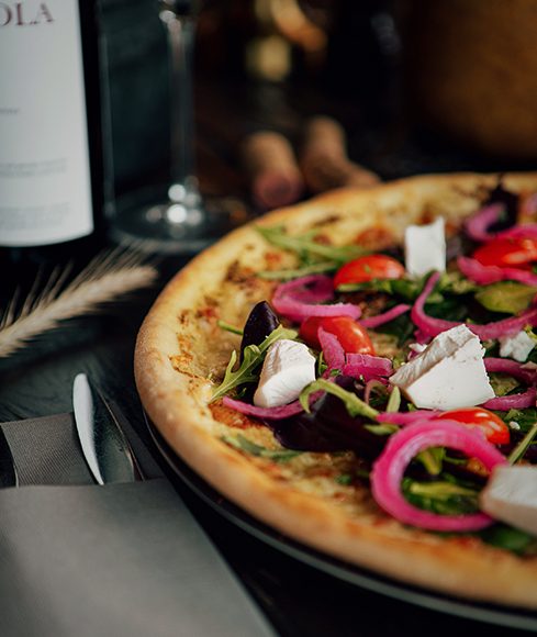Pizza med sallad, rödlök och vit ost på ett mörkt bord